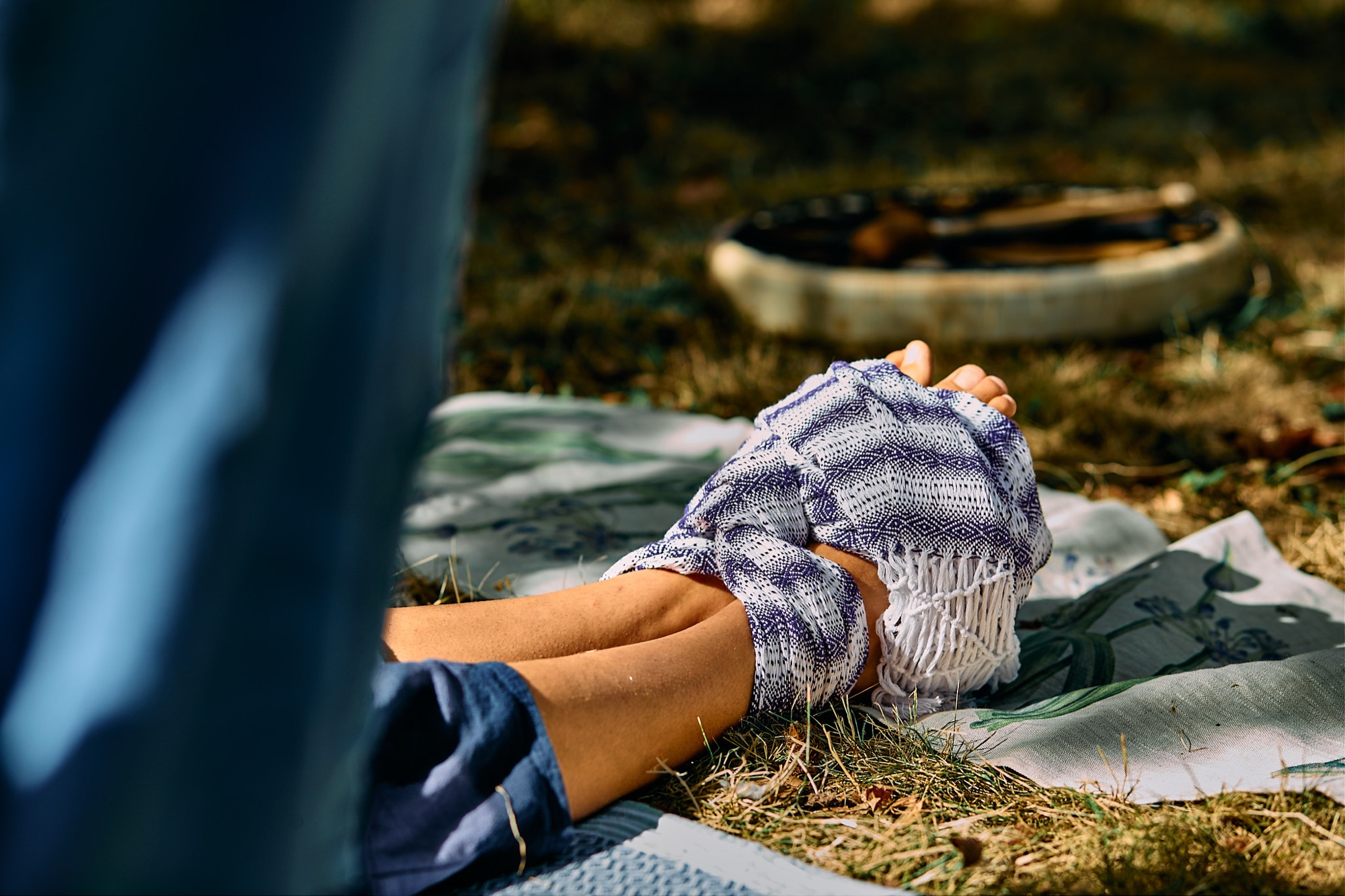 Feet bound in a woven scarf, resting on the grass beside a frame drum